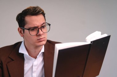 Caucasian blond man dressed in a brown jacket and white shirt looking confused while reading a book. Elegant man reading a book. Business man with confused expression.