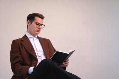 Intellectual man dressed in a suit and glasses reading book sitting on a white background. Elegant business man reading his book. University professor with a book in his hands. High quality photo