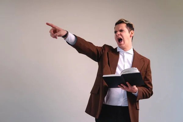 Caucasian blond man dressed in a suit and with a book in his hand. The man is shouting euphorically and pointing somewhere. Annoyed lawyer pointing. Very expressive teacher. High quality photo