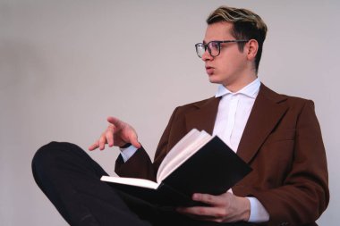 Lawyer sitting in front of a white background talking. Business man sitting with the black book on him. Teacher dressed in a suit presenting a topic. Elegant man dressed in jacket, shirt and glasses