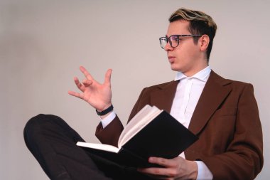 Elegant man with a book gesturing with his hand. School teacher speaking from his chair. Business man on a white background. High quality photo