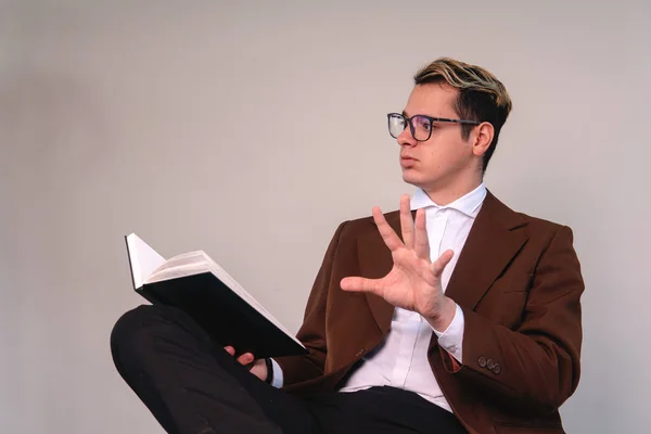 A seated man gesturing to stop. Elegant man with raised hand. Man in a suit, sitting, reading a book. A man in a suit on a white background sitting on a chair. High quality photo