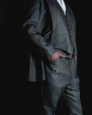 Man dressed in gray suit with his hands in his pockets. Man in a suit posing on a black background. Unrecognizable stylish man posing. Businessman. High quality photo