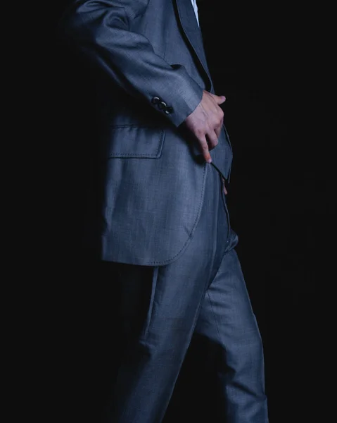 Waist of a man in a suit on a black background. Gray colored suit of an elegant man walking. Unrecognizable man in brown suit walking on dark background. High quality photo