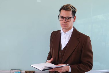 Teacher in front of the class explaining a topic. An elegant man giving a class. University professor with a book in his hand. High quality photo