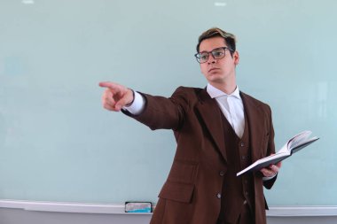 University professor with the white board behind giving a class pointing somewhere. Elegant man in a suit pointing at the students at him. Teacher giving class. High quality photo
