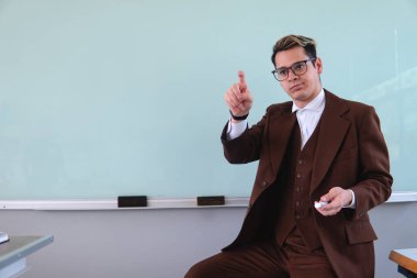 A teacher in a suit pointing towards the class. Teacher in front of the room working with the blackboard behind. High quality photo