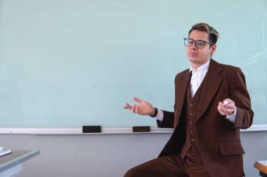Teacher sitting in front of the class with a confused expression. Professor dressed in a brown suit, a shirt and glasses. Elegant man working as a teacher. High quality photo