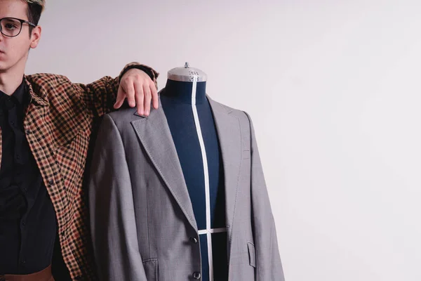 Clothing designer leaning on mannequin with a suit. Blond Caucasian clothing designer dressed in a nice jacket and glasses. Mannequin with a gray jacket. High quality photo