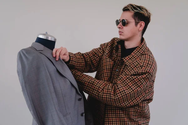 A young fashion designer at work in a gray suit. Caucasian blond clothing designer dressed in a yellow suit and black glasses working on a mannequin. High quality photo