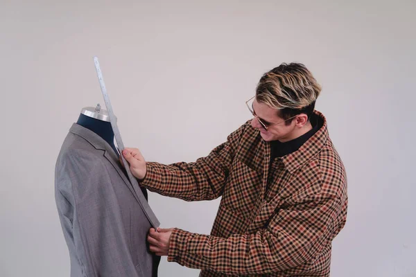Tailor working on a white isolated background. Fashion designer at work in a gray suit. Caucasian and blond man working as a tailor. Fashionably dressed man. High quality photo