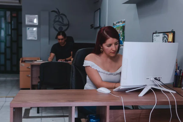 Travel agents working at their desks with their computers. A red-haired woman and a man in a black shirt working in an office. High quality photo