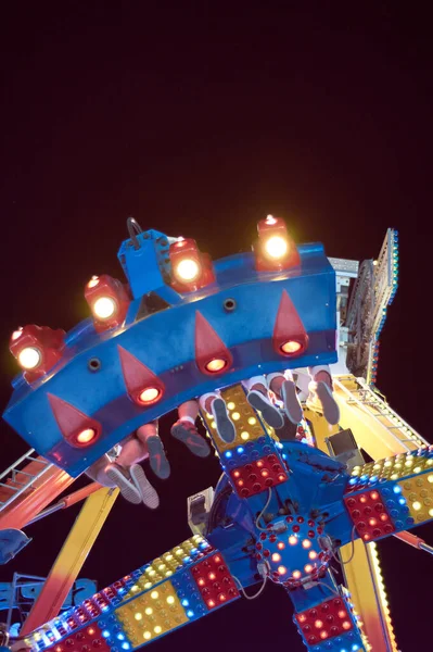 Detail of legs of people sitting on a fairground attraction at night.