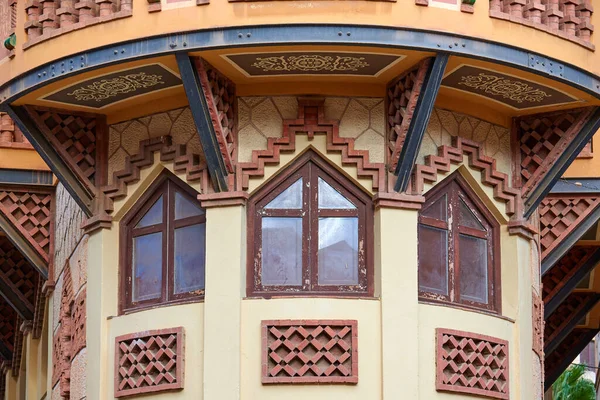 Triangular windows in a circular building with iron beams and flower decorations on the facade