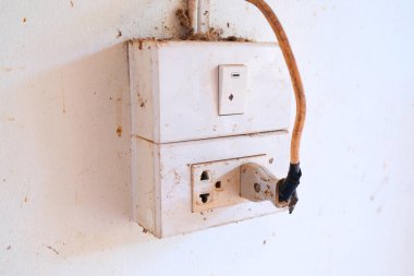 Eski elektrik şalteri ve kablolu elektrik prizi siyah bantla sarılı. Beyaz duvarda hasar var. Evinizde ya da ofisinizde elektrik kullanmanın tehlikeleri.