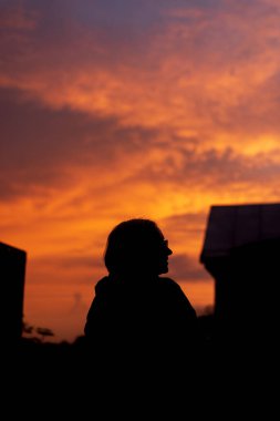 Gün batımının çatısında sırt çantalı bir adamın silueti.