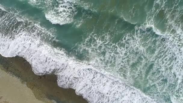 海浪从上方滚来.蓝色碧绿的大海，浪花汹涌，雪白的海水，自上而下的4k无人机视野。阳光灿烂的日子在海面上.巨大的海浪冲击着海岸线.强烈的海浪 — 图库视频影像