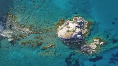 Güneşli bir günde, Turkuaz sularındaki kayalıkların havadan görünüşü. Okyanus dalgaları güzel bir sahil aracının 4K görüntüsü. Yalnız dağ kayasına çarpan deniz, Kıbrıs 'ta turizm beldesi