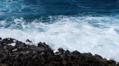 Tehlikeli kayaların üzerinden geçen dalgalar, Deniz fırtınası konsepti, güneşli deniz manzarası, yıkıcı ve muhteşem, okyanus dalgaları kıyıdaki kayalara çarpıyor ve bir su patlaması yaratıyor, 4k