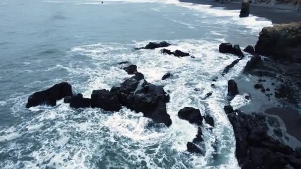 Flygfoto över vågorna bryter på stenar i ett blått hav. Havsvågor på vacker strand, Fåglar syn på havet vågor kraschar mot en tom sten klippa uppifrån, Island — Stockvideo