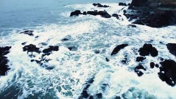 Aerial top view of waves break on rocks in a blue ocean. Sea waves on beautiful beach, Birds eye view of ocean waves crashing against an empty stone rock cliff from above, Iceland — Vídeo de Stock