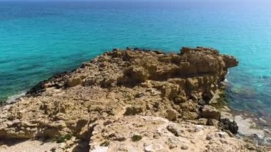 Yeryüzünün kıyısındaki hava manzarası, turkuaz sakin deniz dalgaları kayalık bir uçuruma, okyanus esintisine, saflığa ve dokunulmamış doğaya, jeolojik harikaya, Kıbrıs 'a çarpıyor