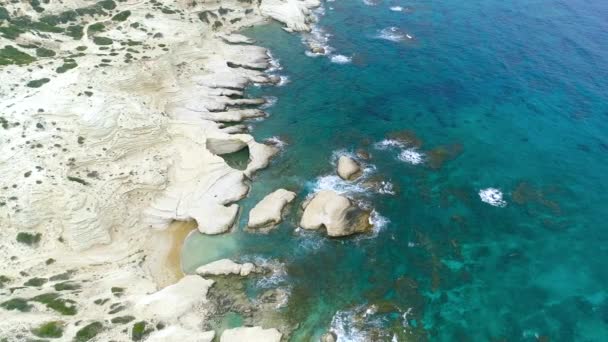 鳥の目のビューから海の海岸線、青い海の波は、美しいビーチの空中ビュードローン4kショット、クリアターコイズブルーの水と白い岩の岩の上に岩の海岸を洗う。キプロス — ストック動画