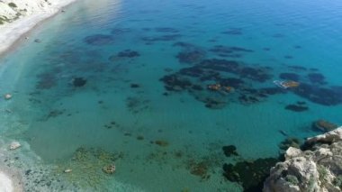 Dalgaların yukarıdaki hava manzarası mavi bir okyanusta sahile çarpıyor. Sakin deniz, güzel sahil manzaralı insansız hava aracı görüntüsü. Kuş bakışı okyanus dalgalarının boş kaya kayalıklarına çarptığını görür.