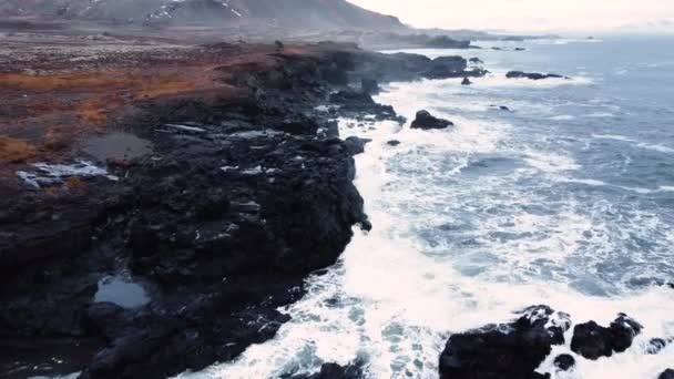 Dalgaların yukarıdan görünüşü mavi bir okyanusta kayalara çarpıyor. Güzel sahilde deniz dalgaları, okyanus dalgalarının manzarası yukarıdaki boş kaya uçurumuna çarpıyor, İzlanda — Stok video
