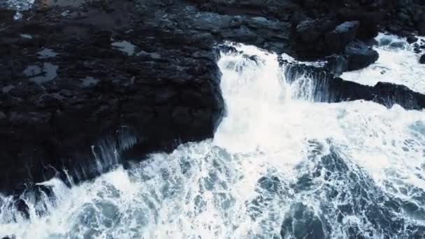 Górny widok fal rozbija się na skałach w błękitnym oceanie. Fale morskie na pięknej plaży, Widok z lotu ptaka na fale oceaniczne uderzające o pustą skałę skalną z góry, Islandia — Wideo stockowe