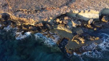 Kayalık Kıyı Hattı üzerinde Mavi Akdeniz ile birlikte Uçan Okyanus Suyu Gün Batımında Güneş 'e Doğru. Kuş Gözü Görünümü 4K Sinematik İnsansız Hava Aracı. Deniz kıyısının üzerinde Gökyüzünden, Kıbrıs