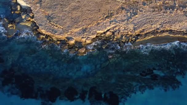 Sziklás part felett repül, sziklák a kék tengernél, óceáni táj naplementekor. Madártávlat 4K Cinematic Drone Footage. Tengeri part a levegőből, Ciprus — Stock videók