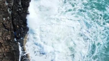 Dalgaların hava görüntüsü mavi bir okyanusta kayalara çarpıyor, deniz dalgaları güzel plajlarda kuşların gözü okyanus dalgaları yukarıdaki boş kaya kayalıklarına çarpıyor, Kıbrıs