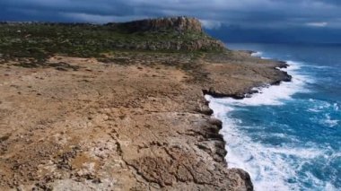 Deniz kayalık sahili yıkar, havadan çekilen karenin üstünde, sahil şeridinde uçar, Kayalıklarda Mavi Saf Suyla, Okyanusta güneşli havada. Kuş Gözü Görünümü 4K Sinematik İnsansız Hava Aracı. Havadan Gelen Sahil, 