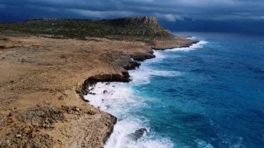 Deniz kayalık sahili yıkar, havadan çekilen karenin üstünde, sahil şeridinde uçar, Kayalıklarda Mavi Saf Suyla, Okyanusta güneşli havada. Kuş Gözü Görünümü 4K Sinematik İnsansız Hava Aracı. Havadan Gelen Sahil, 