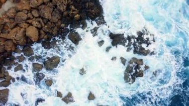 Deniz kayalık sahili yıkar, havadan çekilen karenin üstünde, sahil şeridinde uçar, Kayalıklarda Mavi Saf Suyla, Okyanusta güneşli havada. Kuş Gözü Görünümü 4K Sinematik İnsansız Hava Aracı. Havadan Gelen Sahil, 