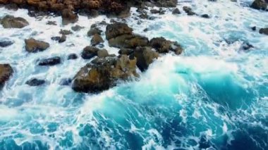 Deniz kayalık sahili yıkar, havadan çekilen karenin üstünde, sahil şeridinde uçar, Kayalıklarda Mavi Saf Suyla, Okyanusta güneşli havada. Kuş Gözü Görünümü 4K Sinematik İnsansız Hava Aracı. Havadan Gelen Sahil, 