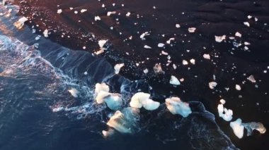 Saf mavi okyanus dalgaları ve ışık yansımaları İzlanda 'daki volkanik plajda buzdağlarını ezer. Yüksek kaliteli 4K görüntüler.