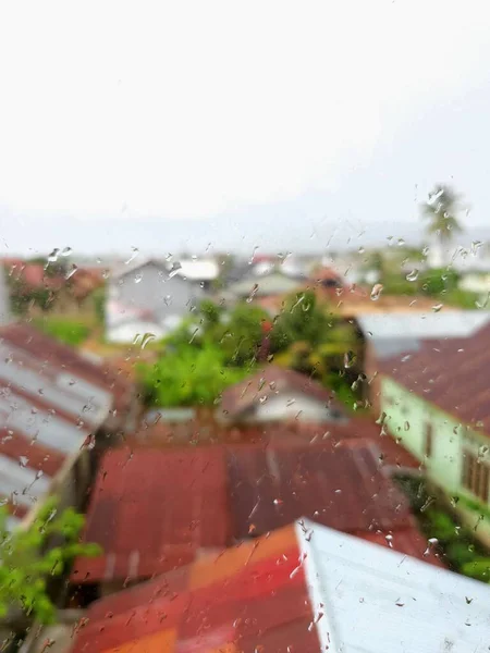 Raindrops on a glass surface with a residential roof background