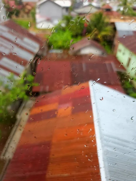 Raindrops on a glass surface with a residential roof background