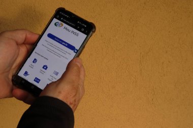 Taubate, SP, Brezilya - Temmuz 07 2022: ekranda INSS sitesi olan akıllı telefonu tutan eller. Sarı arka plan. Gölgeler.