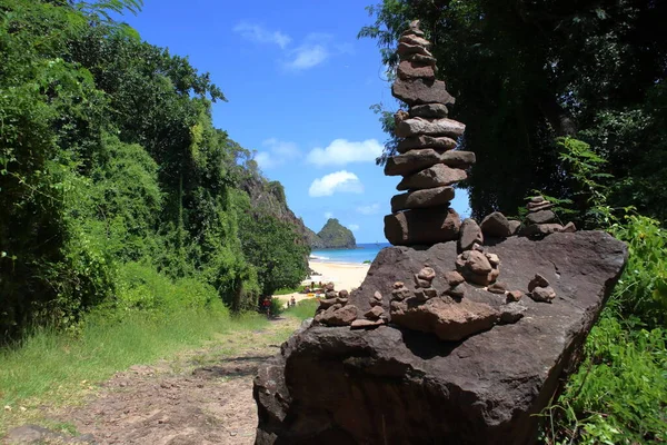 Rock cairn or stack at trail to Cacimba do Padre beach, with Two Brothers Hills at background. Sunny august day. Forest.