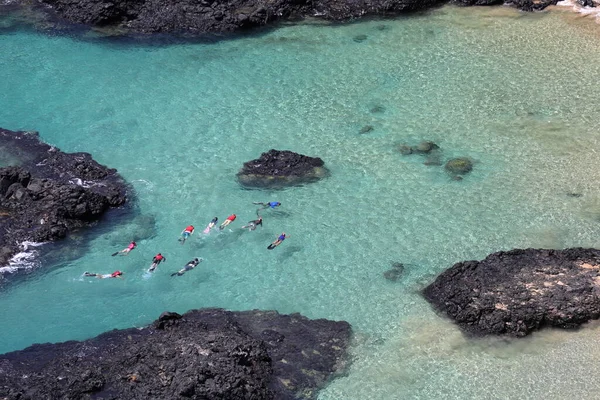 People snorkelling. View towards the vertical rock cliffs of Baia dos Porcos, Pigs Bay, on the remote island paradise of Fernando de Noronha off the coast of Pernambuco, Brazil. . High quality photo