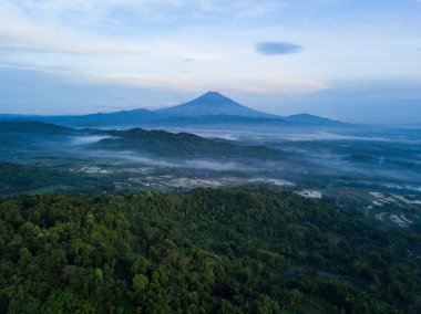 Sabahları tepede ağaçların yoğunluğuyla kaplı Sumbing Dağı 'nın drone fotoğrafı. Orta Java, Endonezya