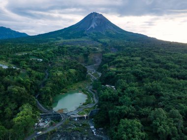 Bebeng Nehri ile Merapi Dağı manzarası ve su tutan bir göl, gökyüzü bulutlu görünüyor. Gölün etrafını saran ağaçlarla dolu orman bitkileri. Bego Pendem, Merapi Dağı