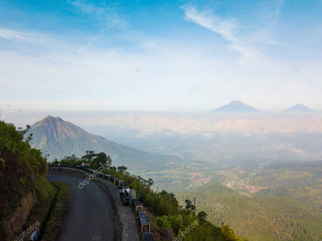 Drone photo of the road on the slopes of a mountain and surrounded by dense forest with Andong Mountain on the background. It located in Mount Telomoyo in clear weather, central java, Indonesia