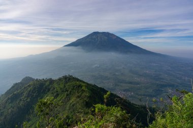 Çimenli, ağaçlı, ön planda ve bulutlu bir dağın zirvesine bakın. Merbabu Dağı adında bir dağ. Bu görüntü Endonezya 'nın merkezindeki Telomoyo Dağı' nın zirvesinden alındı.