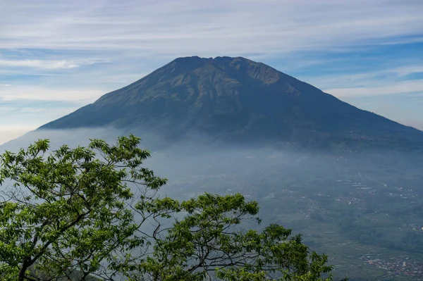 Çimenli, ağaçlı, ön planda ve bulutlu bir dağın zirvesine bakın. Merbabu Dağı adında bir dağ. Bu görüntü Endonezya 'nın merkezindeki Telomoyo Dağı' nın zirvesinden alındı.