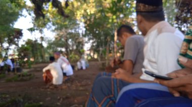 İslami cenaze töreninde beyaz başparmak taşlarıyla arka planda dua eden insanların odaksız fotoğrafı.