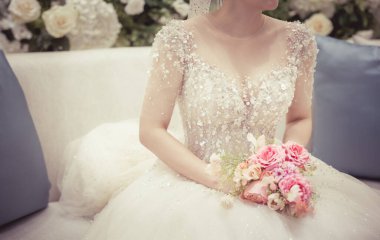 Gelin oturuyor ve elinde düğün buketini tutuyor. Detaylı görüntü kesilmiş..